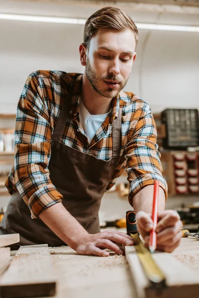 Selective focus of woodworker holding pencil while measuring wooden plank — Stock Photo