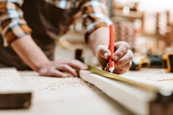 Cropped view of man holding pencil near wooden plank and measuring tape — Stock Photo