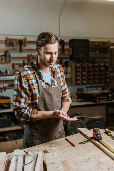 Handsome woodworker standing near table with wooden planks and measuring tape — Stock Photo
