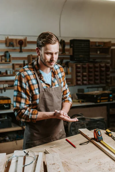 Schöner Holzarbeiter, der neben einem Tisch mit Holzbohlen und Maßband steht — Stockfoto