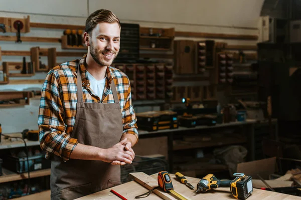 Travailleur du bois heureux avec les mains serrées debout près de la table avec des outils — Photo de stock