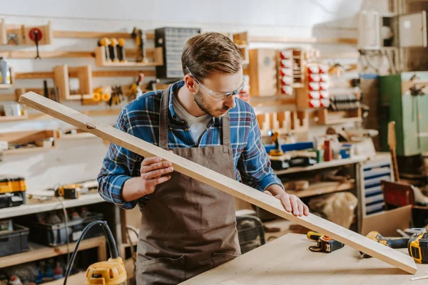 Carpinteiro bonito em óculos segurando prancha de madeira — Fotografia de Stock