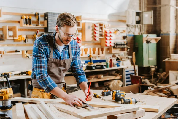 Handsome carpenter in goggles holding pencil in carpentry shop — Stock Photo