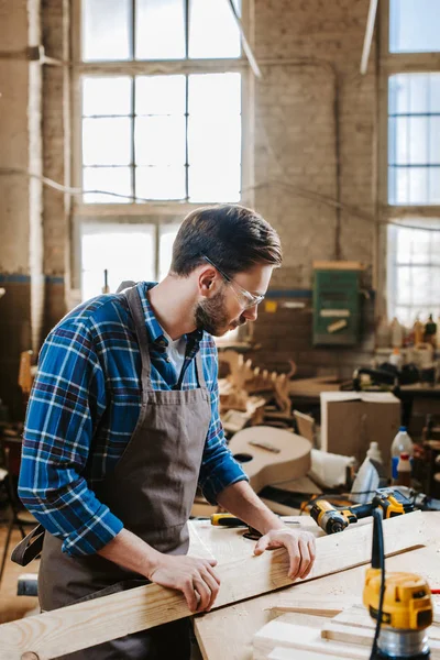 Selective focus of bearded woodworker holding plank in workshop — Stock Photo