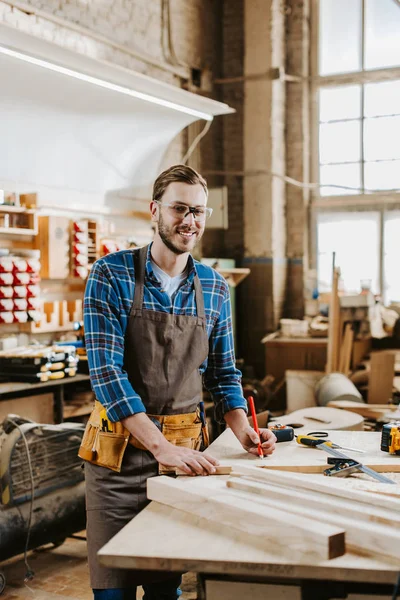 Selective focus of happy woodworker holding pencil near planks — Stock Photo