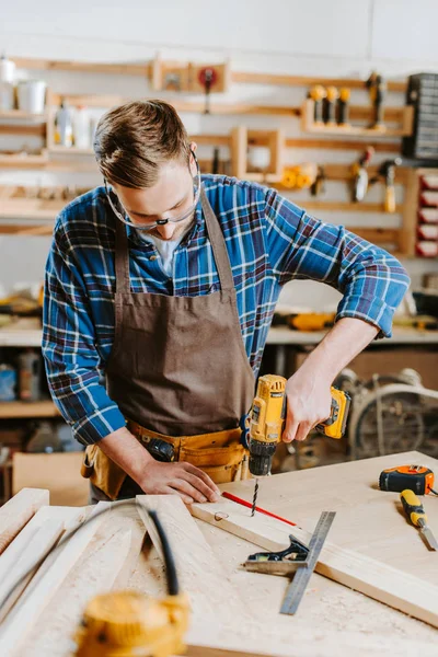 Foco seletivo de carpinteiro em óculos e avental segurando martelo broca — Fotografia de Stock