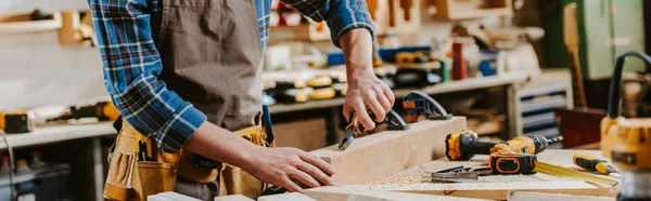 Panoramic shot of carpenter holding pliers near wooden dowel — Stock Photo