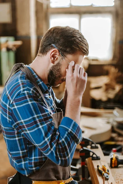 Charpentier couvrant le visage tout en touchant googles en atelier — Photo de stock