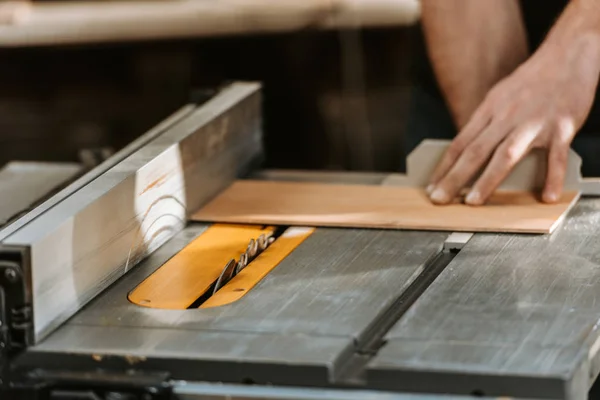 Cropped view of carpenter holding wooden plank near circular saw — Stock Photo