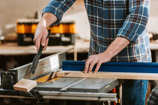 Cropped view of carpenter holding plank near circular saw — Stock Photo