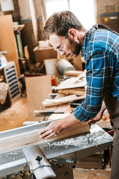 Side view of woodworker in apron holding plank near circular saw — Stock Photo