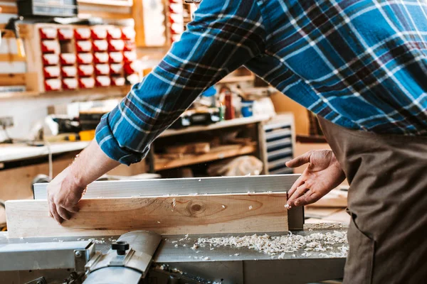 Cropped view of woodworker holding plank near circular saw in carpentry shop — Stock Photo