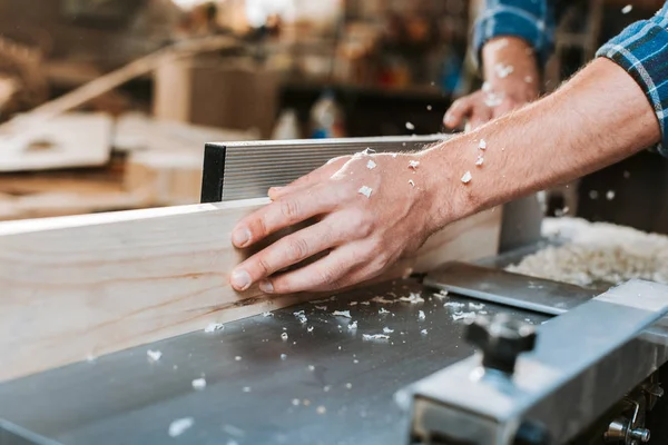 Vista ritagliata del falegname che tiene tavola di legno vicino sega circolare in falegnameria — Foto stock