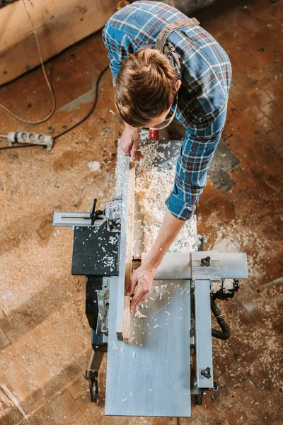 Top view of carpenter holding plank near circular saw in carpentry shop — Stock Photo