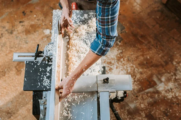 Top view of carpenter holding plank near circular saw in workshop — Stock Photo