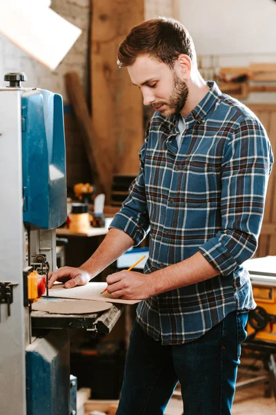 Selektiver Fokus des gutaussehenden Tischlers, der Bleistift in der Werkstatt hält — Stockfoto