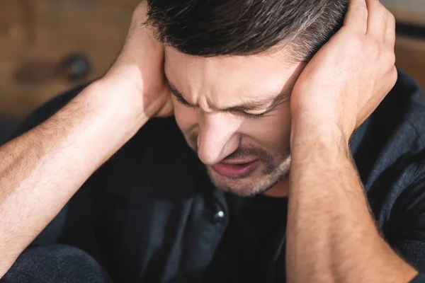 Hombre guapo en camisa negra con dolor de cabeza tocando la cabeza en el apartamento - foto de stock