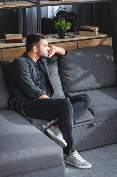 Високий кут зору красивого і стогінного чоловіка, що сидить на дивані в квартирі — стокове фото