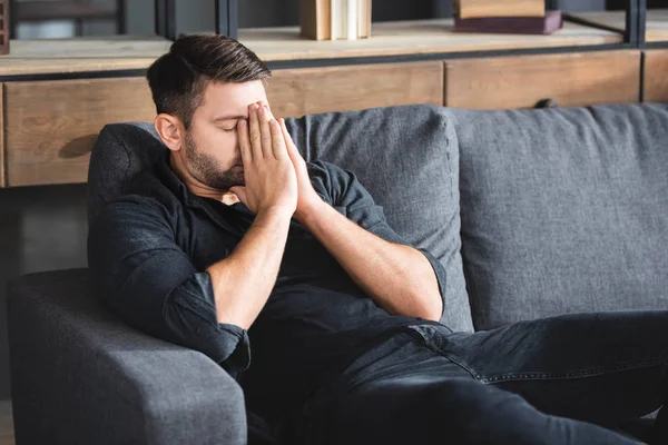 Uomo con mal di testa seduto sul divano e viso oscuro in appartamento — Foto stock