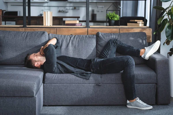 Вид збоку красивого чоловіка з головним болем, що лежить на дивані в квартирі — стокове фото