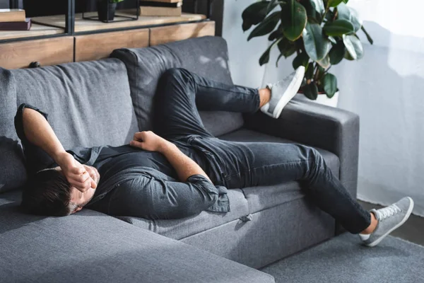 Високий кут зору людини з головним болем, що лежить на дивані в квартирі — стокове фото