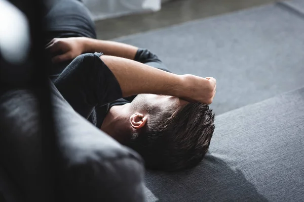 Vista de ángulo alto del hombre con dolor de cabeza acostado en el sofá en el apartamento - foto de stock