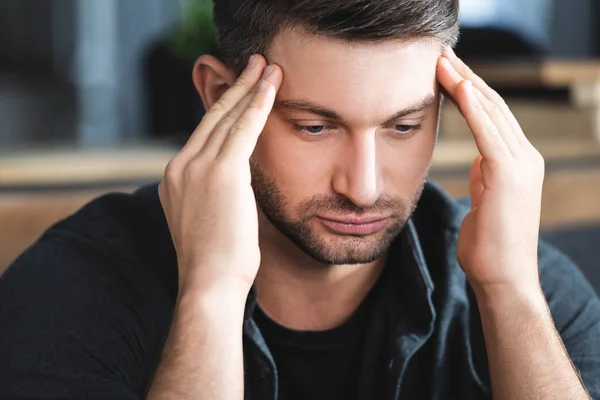 Handsome man with headache touching head and looking down in apartment — Stock Photo