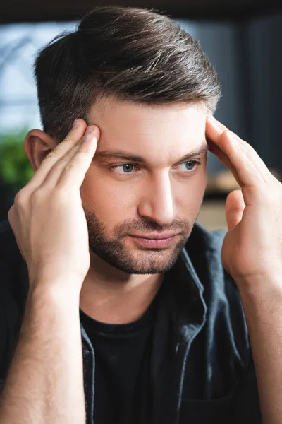 Homem bonito com dor de cabeça tocando a cabeça e olhando para longe no apartamento — Fotografia de Stock
