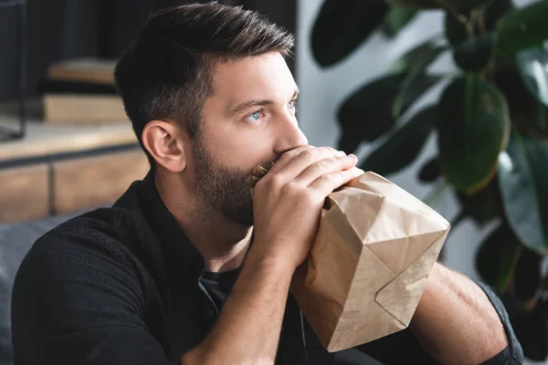 Handsome man with panic attack breathing in paper bag in apartment — Stock Photo