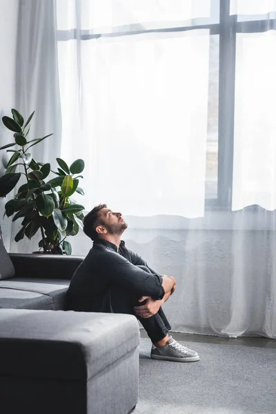 Vista lateral de homem bonito com ataque de pânico abraçando as pernas no apartamento — Fotografia de Stock