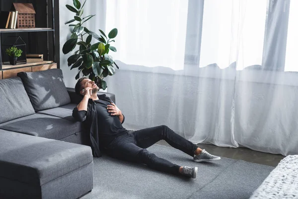 Blick aus der Vogelperspektive auf einen gutaussehenden Mann, der in seiner Wohnung einen Herzinfarkt erleidet und mit dem Smartphone spricht — Stockfoto