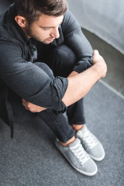 Vue grand angle de l'homme avec attaque de panique étreignant les jambes dans l'appartement — Photo de stock