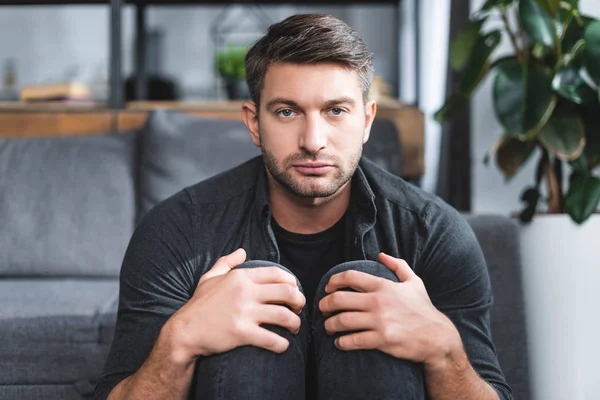 Bonito homem com pânico ataque abraçando pernas no apartamento — Fotografia de Stock