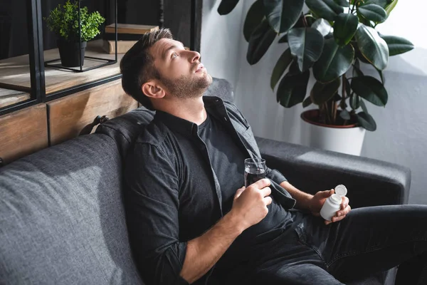 Bonito homem com pânico ataque segurando pílulas e vidro de água no apartamento — Fotografia de Stock