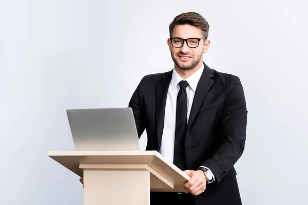 Smiling businessman in suit standing at podium tribune during conference isolated on white — Stock Photo