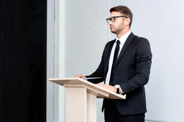 Бизнесмен в костюме стоит на трибуне и смотрит в сторону во время конференции на белом фоне — стоковое фото