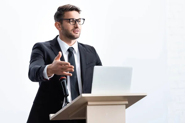 Hombre de negocios en traje de pie en el tribuno podio y hablando durante conferencia aislado en blanco - foto de stock