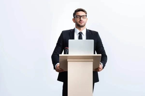 Uomo d'affari in giacca e cravatta in piedi sul podio tribune e guardando lontano durante la conferenza isolato su bianco — Foto stock