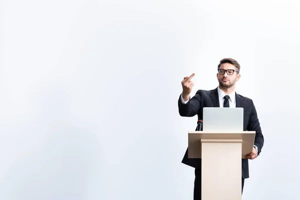 Businessman in suit standing at podium tribune and showing middle finger during conference isolated on white — Stock Photo