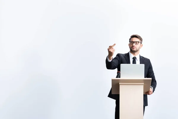 Geschäftsmann im Anzug steht auf der Tribüne des Podiums und zeigt während der Konferenz den Mittelfinger isoliert auf Weiß — Stockfoto