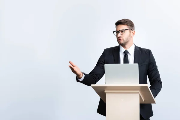 Hombre de negocios en traje de pie en el tribuno podio y hablando durante conferencia aislado en blanco - foto de stock