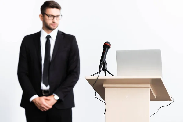 Foco selectivo del tribuno del podio con el ordenador portátil y el micrófono, hombre de negocios en traje sobre fondo aislado en blanco - foto de stock