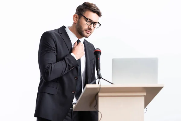 Scared businessman in suit standing at podium tribune and touching tie during conference isolated on white — Stock Photo