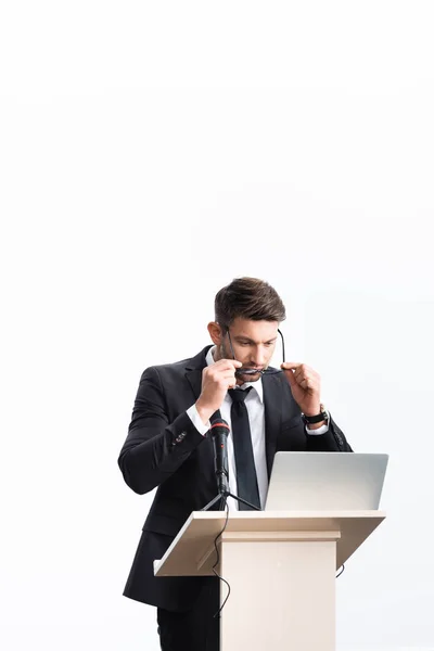 Businessman in suit standing at podium tribune and wearing glasses during conference isolated on white — Stock Photo