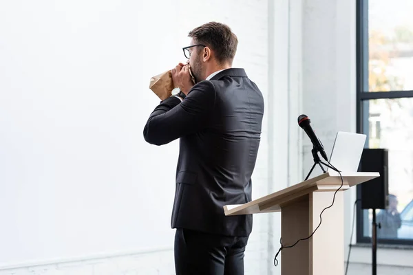 Назад вид испуганного бизнесмена в костюме, дышащего бумажным пакетом во время конференции — Stock Photo