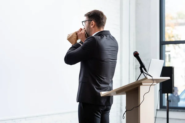 Vue arrière de l'homme d'affaires effrayé en costume respirant dans un sac en papier pendant la conférence — Photo de stock