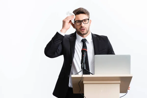 Asustado hombre de negocios en traje de pie en el tribuno podio y la celebración de la servilleta durante la conferencia aislado en blanco - foto de stock