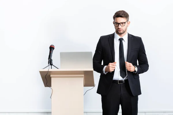 Homem de negócios de terno de pé perto tribuno pódio durante conferência isolada em branco — Fotografia de Stock
