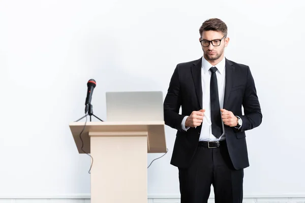 Uomo d'affari in giacca e cravatta in piedi vicino al podio tribune durante la conferenza isolato su bianco — Foto stock