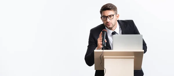 Tiro panorâmico de empresário de terno em pé no tribuno pódio e falando durante conferência isolada em branco — Fotografia de Stock